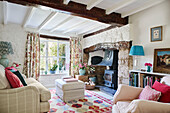 Floral curtains at window with footstool and woodburner in cottage living room, UK