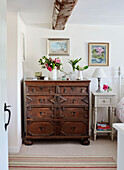 Antique wooden chest of drawers with cut flowers in cottage bedroom, UK