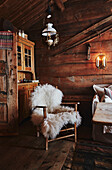 Mit Schafsfell bezogener Sessel in einer Ecke des Wohnzimmers einer Holzhütte in den Bergen von Sirdal, Norwegen