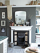 Vintage fireplace and mirror with books in muted grey living room of Winchester home, Hampshire, UK