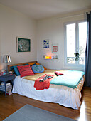 Double bed with an assortment of cushions at window of family home, France