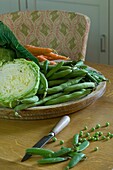 Stilllebene mit Karotten, Kohl, grünen Erbsen und Messer auf dem Tisch