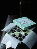 Opened box of chocolates resting on an arm of a leather chair