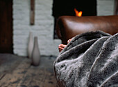 Person under a blanket on a sofa next to a lit open fire in the living room