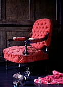 A period vintage style worn armchair in a dark wood panelled room with clothes and shoes on the floor