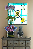 Fresh cut flower display on a chest of draws with a stained glass window