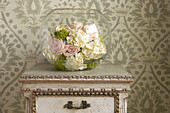 Bowl of fresh cut flowers displayed on a small chest of draws with patterned wallpaper