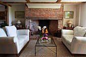 Matching sofas and glass topped coffee table at fireside in Iden farmhouse, Rye, East Sussex, UK