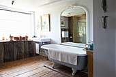 Large arched mirror above freestanding roll-top bath Iden farmhouse, Rye, East Sussex, UK
