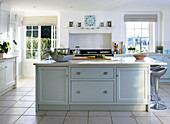 Sunlit kitchen with muted blue kitchen island and tiled floor in Lincolnshire country house, England, UK