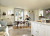 Woman stands at kitchen table in open plan Gloucestershire farmhouse kitchen England, UK