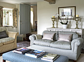 Two seater sofa and ottoman footstool in living room of Gloucestershire farmhouse, England, UK