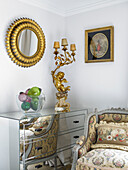Gold leaf mirror frame and lamp on mirrored chest with armchair in room corner city of Bath Somerset, England, UK