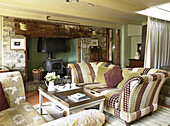 Mit strukturiertem Stoff gepolsterte Sofas und Holzofen im Wohnzimmer eines walisischen Cottage, UK