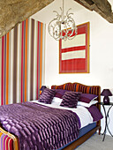Purple bed cover with striped feature wall in bedroom of Welsh cottage, UK