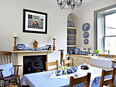 Woodburning stove in fireplace with spotted tablecloth and cushions and decorative plates in city of Bath kitchen Somerset, UK