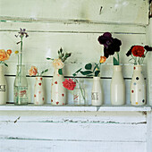 Row of patterned storage bottled lined up on a shelf with flowers placed in them