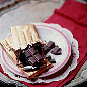 Eine Tafel dunkle Schokolade in geöffneter Goldpapier auf einem Teller
