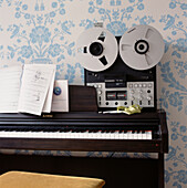 Detail of a piano keyboard and a music recorder in a music room with blue patterned wallpaper