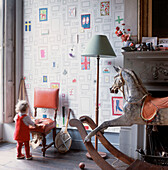 A wallpapered living room with a rocking horse and a small child playing