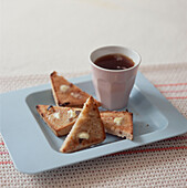 Heißes, mit Butter bestrichenes, getoastetes Früchtebrot auf einem quadratischen Teller mit einer Tasse schwarzem Tee
