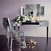 Feminine dressing room with party clothes draped on chair mirrored dressing table and a bunch of pink roses