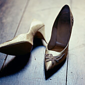 Pair of dressy gold high heeled shoes taken off on a dark wooden floor