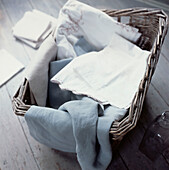 Detail of fabric and linens in a laundry basket on a wooden floor