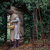 Young woman opening a garden door carrying a trugg