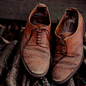 A pair of old worn brown leather shoes on top of a wood pile