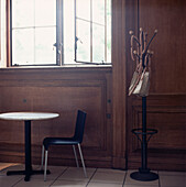 Kleiner runder Tisch, Esszimmerstuhl und Kleiderständer in einem holzgetäfelten Raum