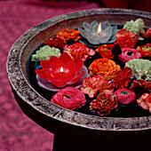 Flower heads and ornamental candles floating in a bird bath