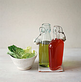 Oil and Vinegar salad dressing bottles with a bowl of fresh lettuce leaves