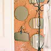 Wallpapered hallway with a collection of mirrors and a coat stand