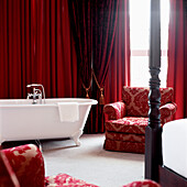 Modernes, rot dekoriertes Schlafzimmer mit gepolstertem Sessel und Badewanne