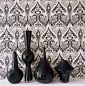 Schwarz-weiß gemusterte Tapete 'Exotic' von Julien Mcdonald mit schwarzen Glaswaren und Keramikvasen in einem Regal