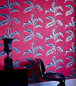 Red bold patterned wallpaper in a living room with black side table chair and urn
