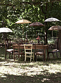 Parasols shading vintage table and chairs in woodland garden, UK
