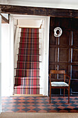 Carpeted staircase with dark wood panelled wall and chequered floor, UK