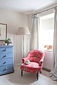 Floral patterned armchair with blue chest of drawers at window in UK home