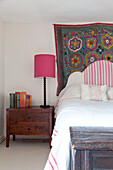 Floral embroidered wall hanging above bed with wooden bedside table in UK home