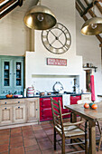 Brass lampshades hang in Surrey barn conversion kitchen with red range oven England UK