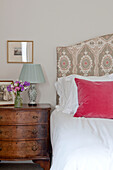 Pink cushion on bed with antique chest of drawers in Wiltshire country house England UK