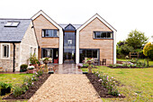 Holzfassade und Terrasse mit Kiesweg an freistehendem Landhaus in Wiltshire, England, UK