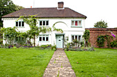 Footpath in lawn to front door of whitewashed Surrey cottage England UK