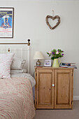 Heart shaped wall hanging above wooden sideboard in bedroom of Surrey cottage England UK
