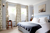 Dark grey blanket on double bed in room with floral patterned curtains contemporary Chelsea home London UK