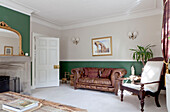 Brown leather sofa and wooden armchair in green living room of Surrey home England UK
