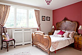 Antique wooden bed at window of red bedroom in Surrey home England UK