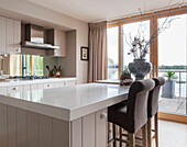 Breakfast bar and stools with patio doors in kitchen of Lakeside home, England, UK